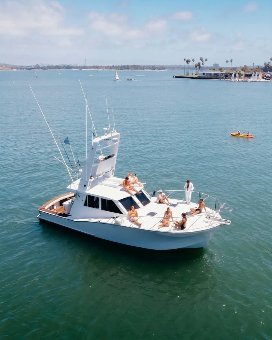 Aerial view of guests sunbathing on Bluebill's bow at anchor in Mission Bay, with sailboats, kayaks and the palm-lined shore behind