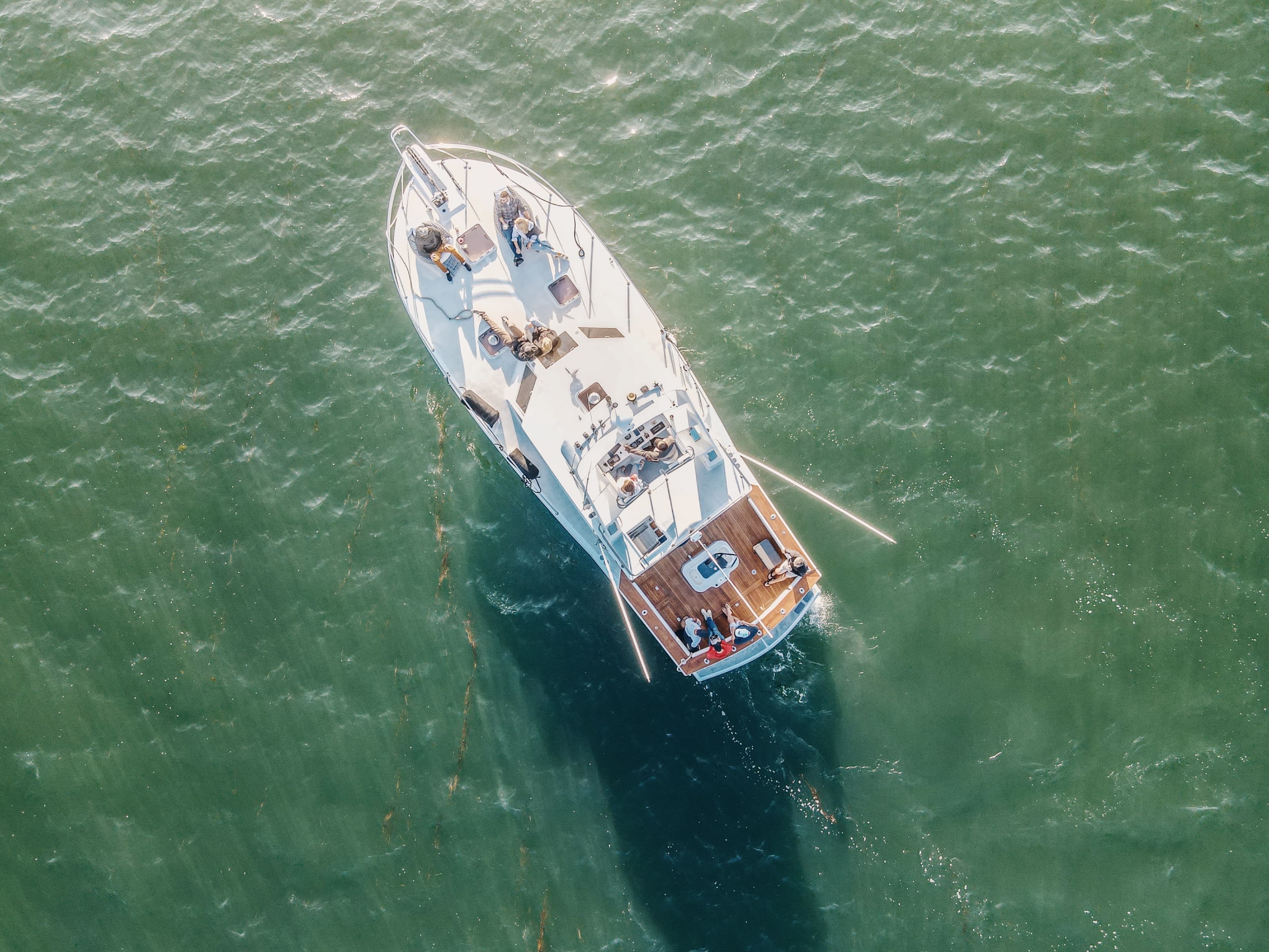 Top-down aerial of Bluebill on green water with guests lounging on the bow and stern decks