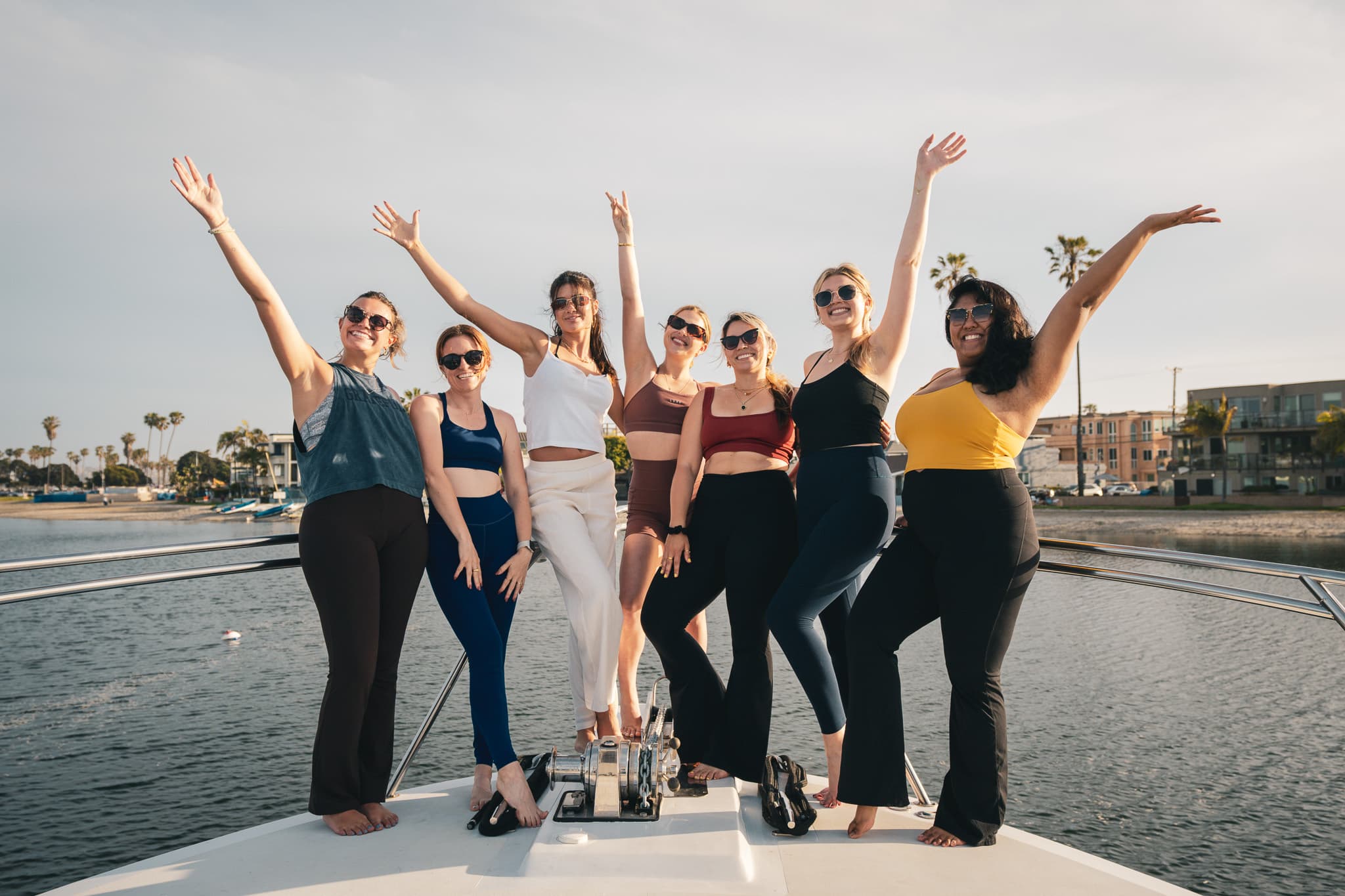 Eight women on Bluebill's bow with arms raised in celebration, bay and palms behind