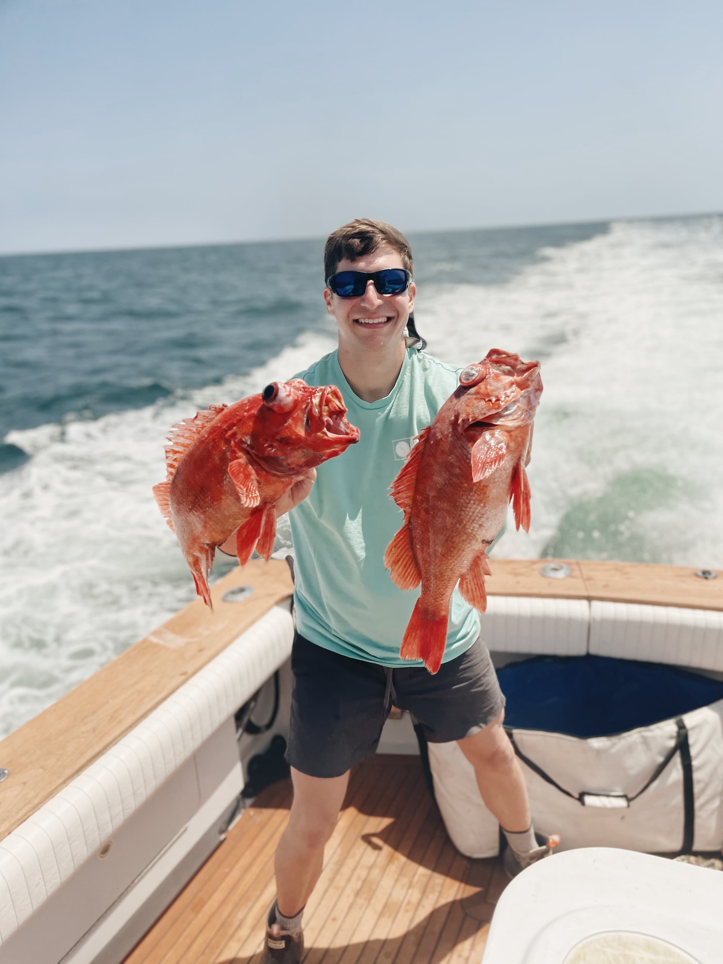 Smiling angler aboard Bluebill holding up two bright red rockfish